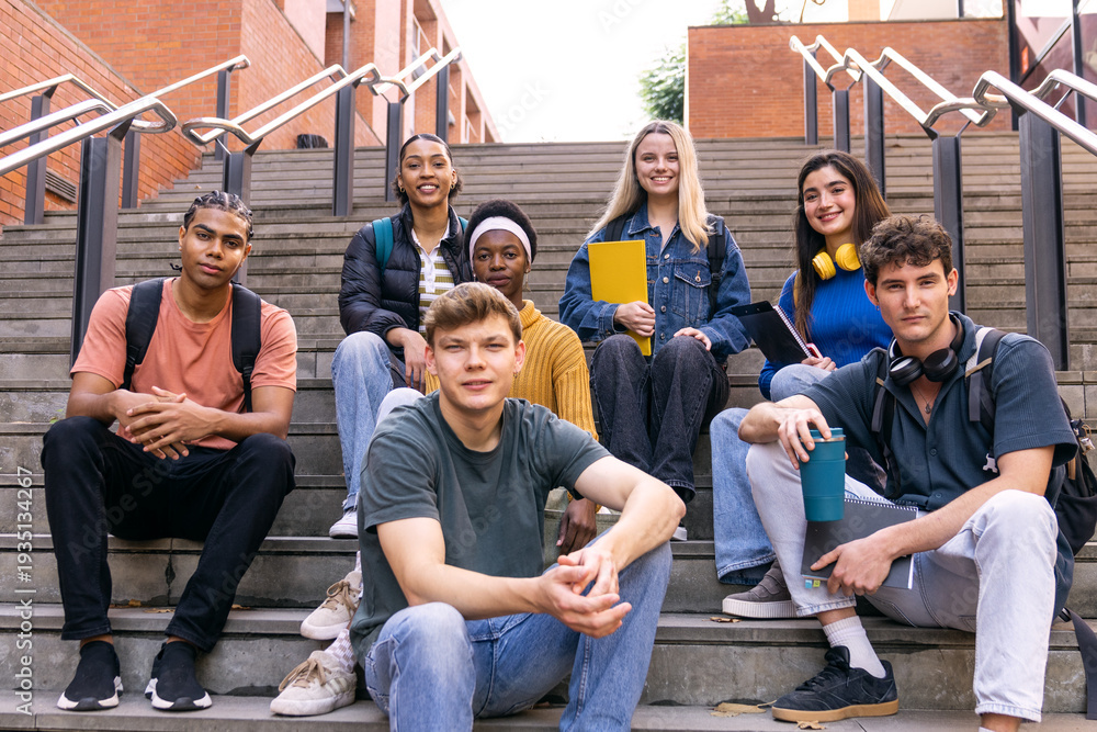 Fototapeta premium Group of diverse university students with backpacks and books sitting on outdoor stairs, showing friendship and education