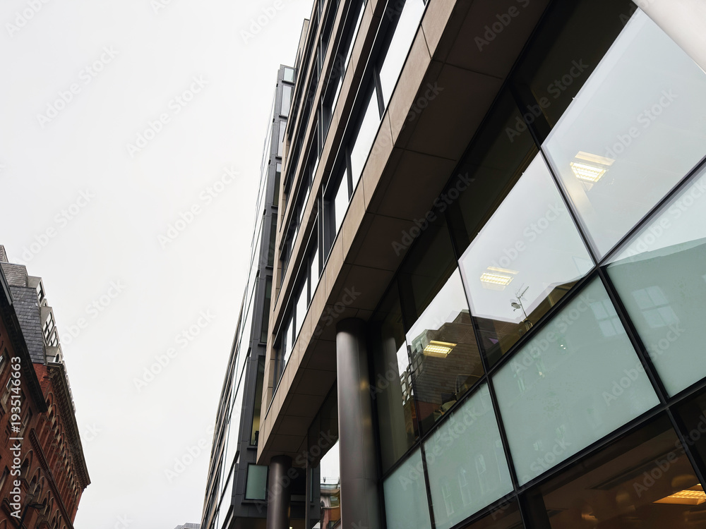 Fototapeta premium Modern glass facade of Manchester office building captured from street level with dramatic perspective
