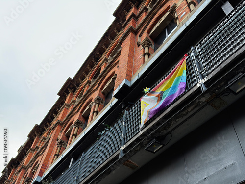 Historic brick building in Manchester with rainbow LGBTQIA flag on balcony and urban facade