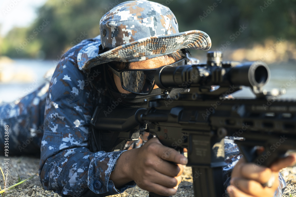 Fototapeta premium Determined military soldier in camouflage aiming rifle with scope. This focused operator lies prone outdoor on combat mission, showing intense concentration and alertness