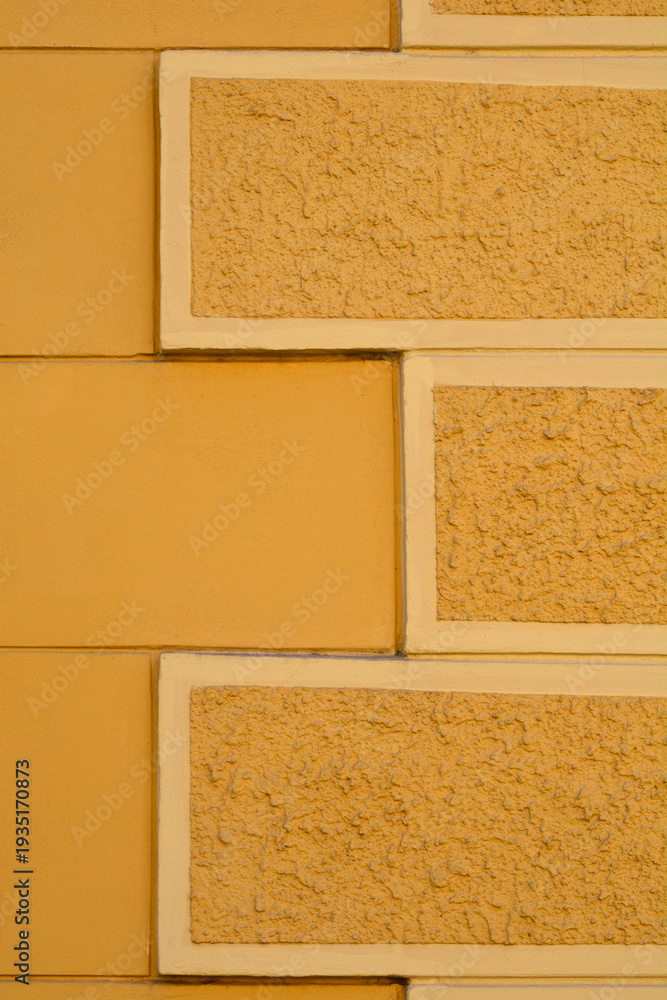 Fototapeta premium A close up of a yellow building facade featuring rectangular decorative elements with a rough mineral texture arranged in a staggered pattern