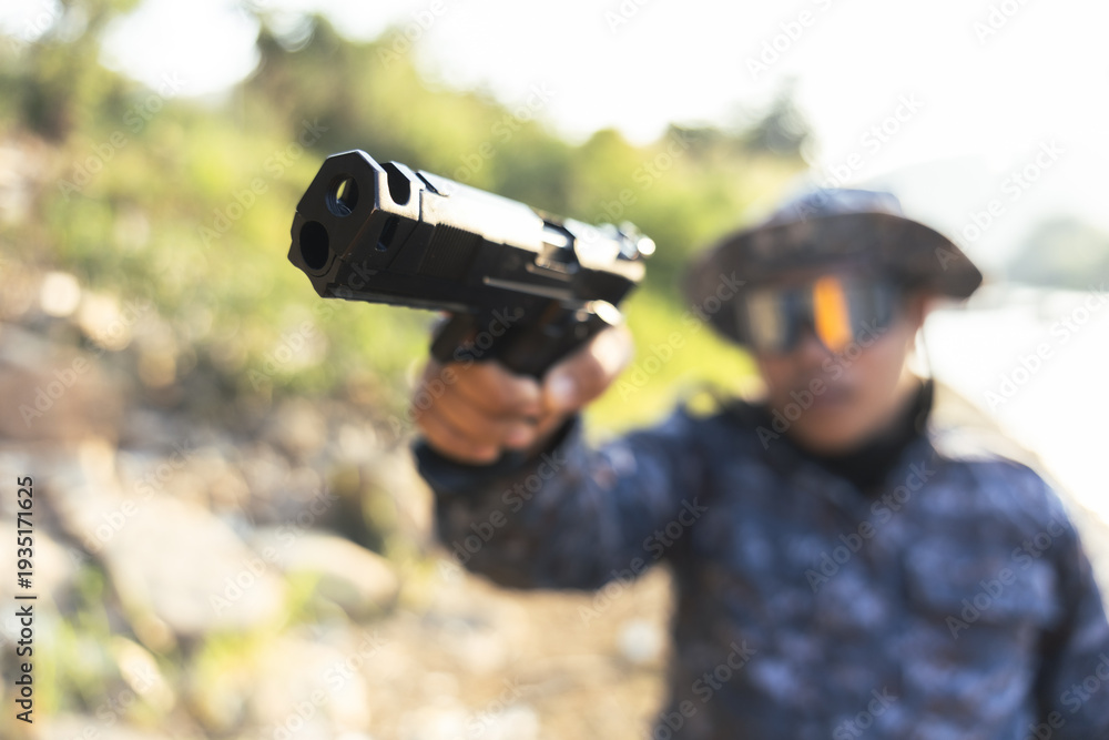 Obraz premium Focused man aiming black handgun, pointing pistol with dangerous and aggressive expression. armed person holds weapon outdoors with serious concentration