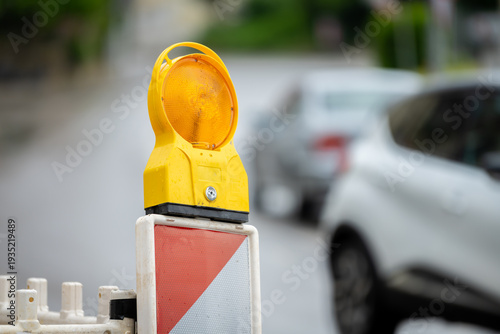 Obraz na płótnie Yellow Barrier Light at Roadwork Site with Out-of-Focus Vehicles in Background,