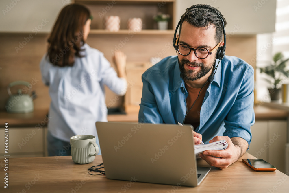 Obraz premium Man working remotely at kitchen counter with partner