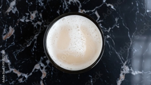 A glass of beer with a frothy head sits on a black marble countertop.