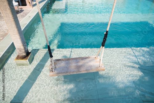 Photos The serene scene of a wooden swing suspended above a crystal-clear swimming pool, inviting relaxation and leisure