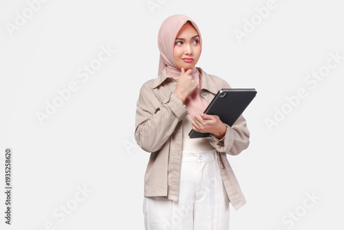 Confused young Asian woman wearing hijab is thinking hard while holding tab document.