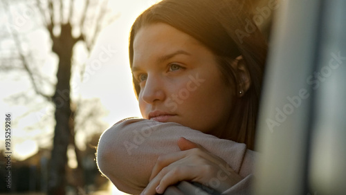 A young woman with long, straight hair sits in a car during a sunlit road trip. She gazes thoughtfully out the window, her hand resting on her knee.