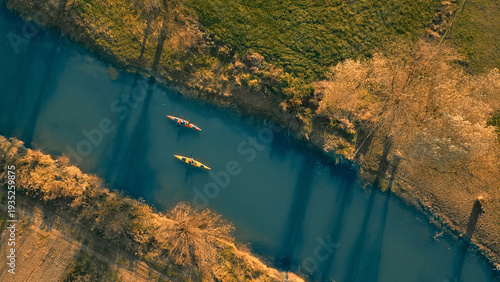 Aerial view of two kayakers on a serene, winding river surrounded by lush greenery and autumn foliage. Captures adventure and tranquility, ideal for travel and sports enthusiasts.