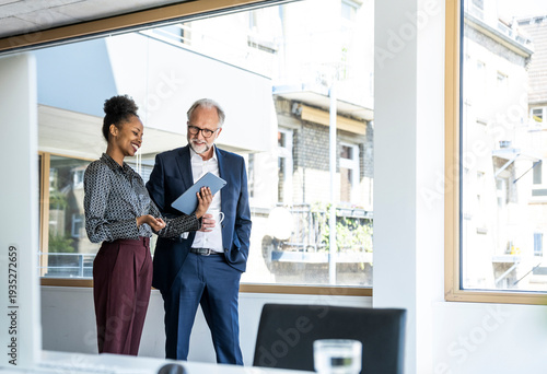 Colleagues communicating and smiling with tablet in modern office