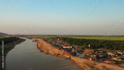 Wallpaper Mural Aerial view of the floating village of Chong Kneas along a riverbank in Cambodia, with boats and houses clustered near the water and lush green fields in the background. Torontodigital.ca