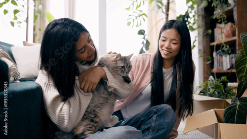 Fotografie Young women bonding with their domestic cat while unpacking boxes, settling into