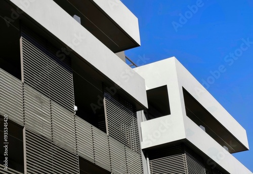 Photo of a minimalist contemporary residential facade featuring deep-set balconies and integrated brise-soleil louvers.