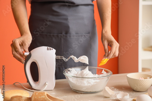 Quadro em tela Woman whipping egg albumen with mixer at table in kitchen, closeup