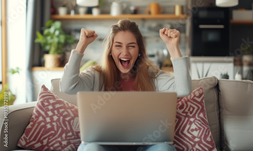 A happy woman celebrating winning or business success working at a laptop at home