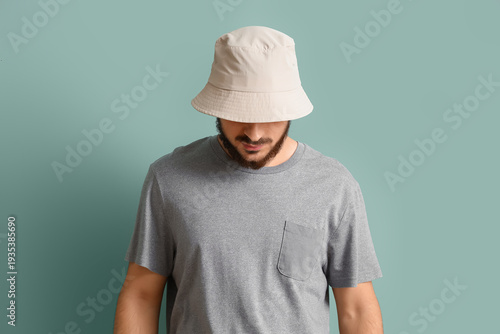 Photos Young bearded man in blank bucket hat and gray t-shirt looking down on pastel bl