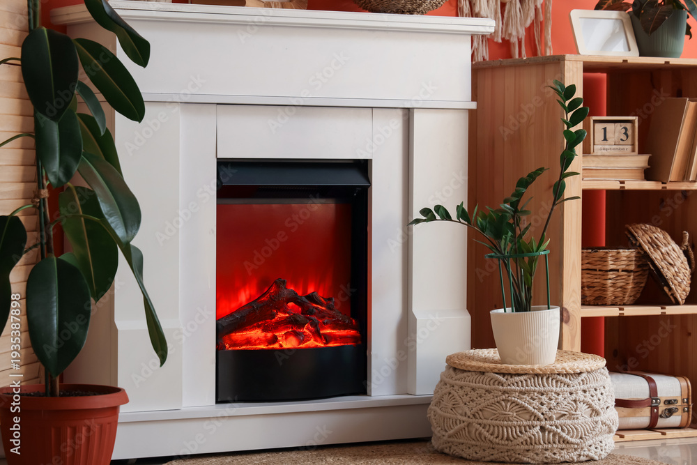 Fototapeta premium Fireplace with folding screen, shelving unit and decor near orange wall in living room