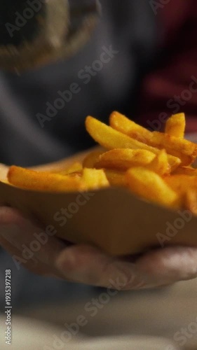 A gloved vendor carefully portions crispy fries into a container at a lively festival food stall, surrounded by excited attendees eagerly waiting for tasty treats and savoring the vibrant atmosphere