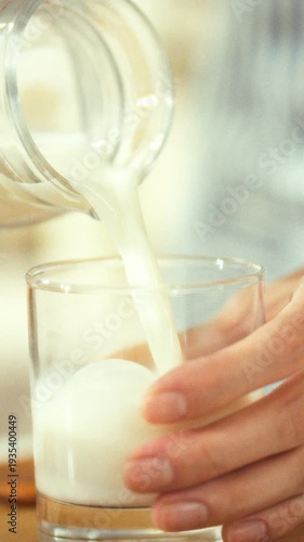 A hand carefully pours chilled milk from a glass bottle into a transparent glass on a wooden table, near a plate of cookies, crafting a warm and welcoming setting for a comforting snack and drink