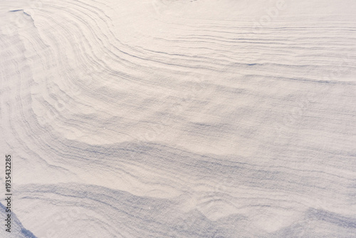 Minimalist frozen landscape texture, layered snow ripples and elegant wind-formed patterns in bright winter conditions.