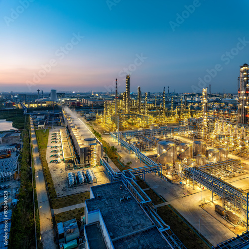 Fotografi Aerial view of a massive petrochemical refinery complex illuminated with lights during sunset, showcasing industrial infrastructure and energy production