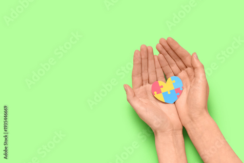 Female hands holding colorful puzzle pieces in shape of heart on green backgr...