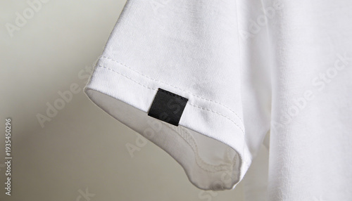 Minimalist white t-shirt sleeve detail with blank black square label attached for branding opportunities on plain garment fabric