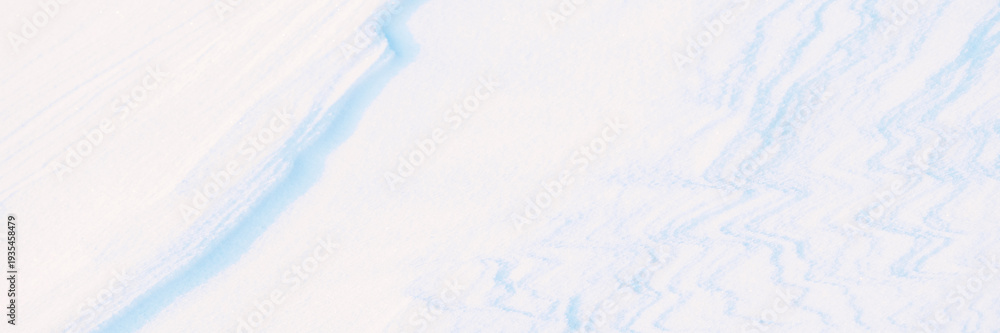 Obraz premium Wide panoramic winter background with snowy ground. Natural snow texture. Wind sculpted patterns on snow surface. Closeup top view with copy space.