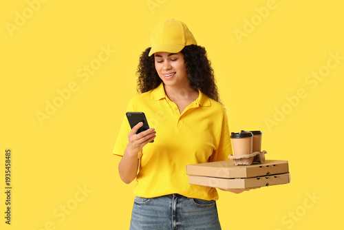 Female African-American courier holding holding mobile phone, paper cups of c...