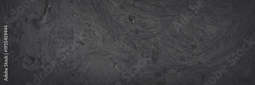 Dark wide panoramic background. Peeling paint on a concrete wall. Faded dark texture of old cracked flaking paint. Weathered rough painted surface with patterns of cracks. Shaded background for design