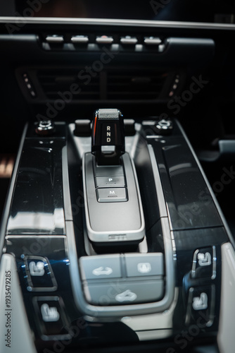 Fotografie Center console of a white Porsche 911 Carrera shows R N D toggle above P and M buttons, glossy black panels with backlit controls, GT inspired trim, and soft showroom lighting