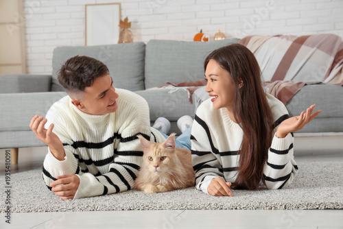 Beautiful young couple with cute Maine Coon cat lying on carpet in living room