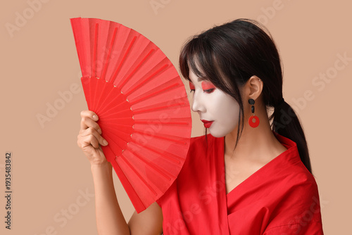 Quadro su tela Beautiful young geisha in traditional clothes with fan on beige background