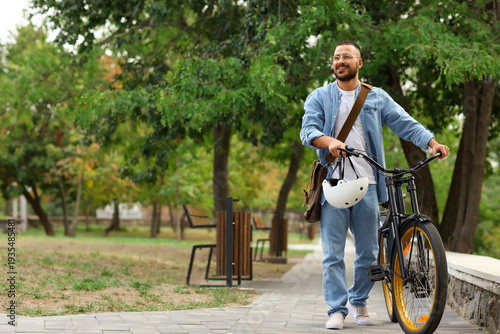 Bild auf Leinwand Young happy man with helmet and bicycle walking in park