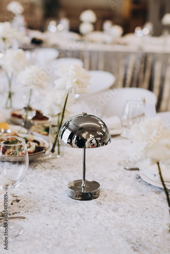 Modern silver cordless lamp on a marble table at an elegant banquet with white flowers and glassware, perfect for luxury interior and event design.