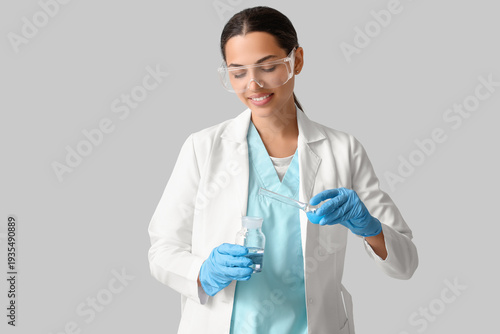 Happy female young scientist with flasks of water samples on grey background
