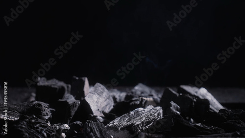 Quadro su tela Low key close up of charcoal chunks in a grill with faint smoke on dark background, ideal for BBQ, heat, fuel and industrial texture concepts
