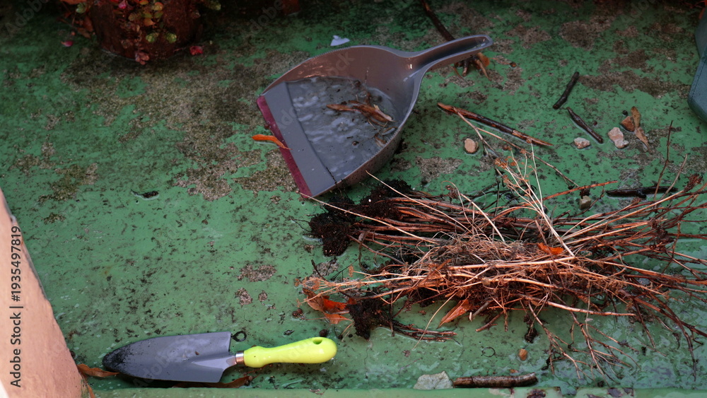 Fototapeta premium Cleaning tools, dry branches, and debris on wet green balcony floor during rain, small gardening shovel and dustpan with water, urban outdoor maintenance