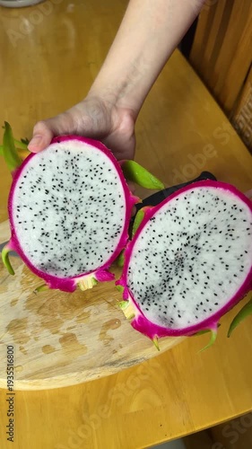 Hands slicing a fresh, vibrant pink dragon fruit on a light wooden cutting board, preparing the healthy tropical pitaya with a sharp knife for culinary use