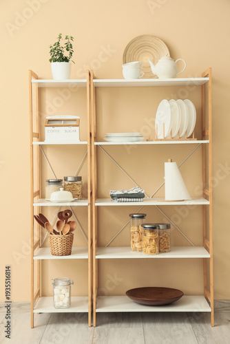 Konstfotografi Shelf unit with kitchen utensils and food near beige wall in room