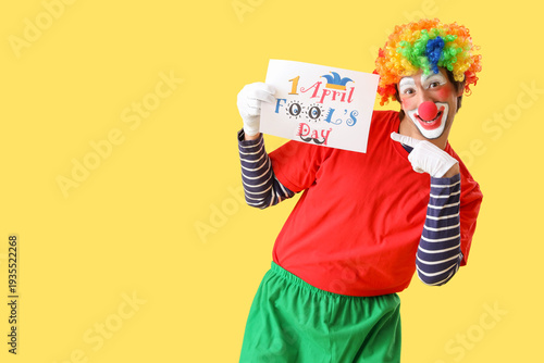 Portrait of clown pointing at poster with text APRIL FOOLS DAY on yellow back...