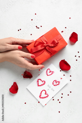 Female hands with red manicure, gift box and festive postcard on white grunge background. Valentine's Day celebration