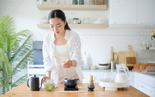 Young woman preparing matcha in bright modern kitchen. Healthy lifestyle and wellness drink concept.