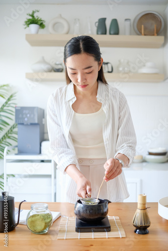 Young woman preparing matcha in bright modern kitchen. Healthy lifestyle and wellness drink concept.