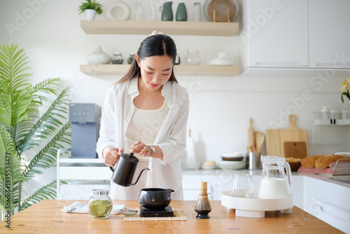 Young woman pouring hot water into matcha bowl in modern kitchen. Healthy lifestyle and wellness drink concept.