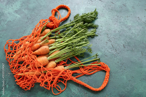 String bag with fresh carrots on green background