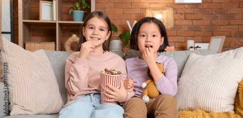 Cute girls with popcorn watching cartoons on sofa at home