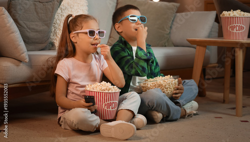 Happy children eating popcorn and watching cartoons at home in evening
