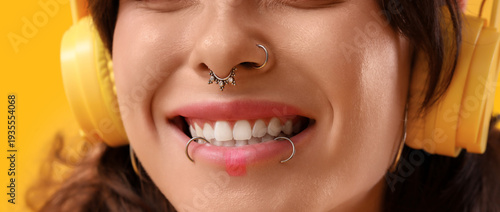 Bild auf Leinwand Young woman with face piercing listening to music on yellow background, closeup