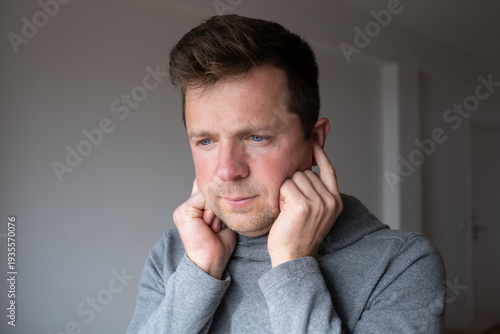 Distressed middle aged man covering his ears with hands, refusing to listen to noise or conflict